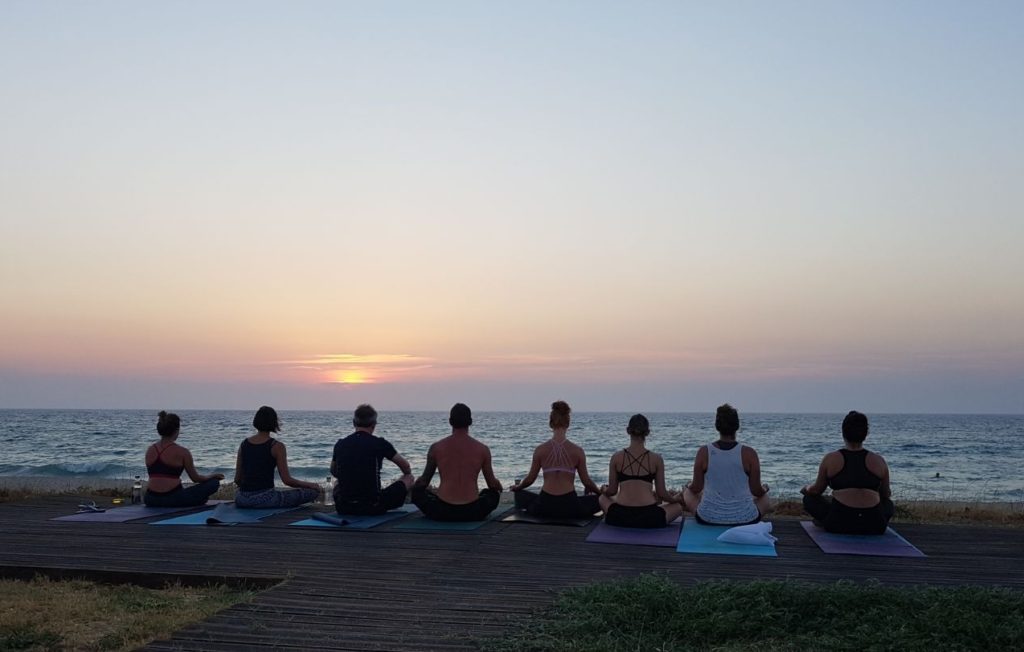 Yoga group on a beach in Corfu, with the sun setting over the sea's horizon
